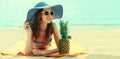 Summer portrait of happy smiling young woman lying on the beach with funny pineapple wearing straw hat Royalty Free Stock Photo