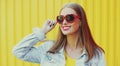 Summer portrait of happy smiling young woman wearing a red heart shaped sunglasses in city over yellow background Royalty Free Stock Photo