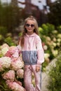 Summer portrait of a smiling girl. Little beautiful girl blonde. Pink flowers on flowerbed. Garden with pink flowers, summer