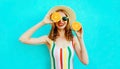 Summer portrait smiling woman holding in her hands two slices of orange fruit hiding her eye in straw hat on colorful blue Royalty Free Stock Photo