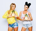 Summer portrait of two cheerful girlfriends, having fun with slice pineapple and smiling. Casual style, bright makeup