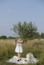 Summer portrait unrecognizable young girl in white dress, hat stands barefoot on blanket.