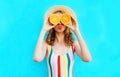 Summer portrait woman holding in her hands two slices of orange fruit hiding her eyes in straw hat on colorful blue Royalty Free Stock Photo