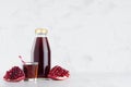 Summer red pomegranate in glass bottle mock up with straw, wine glass, fruit grains on white wood table in light interior. Royalty Free Stock Photo