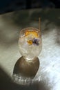 Summer refreshment aperitif cocktail in glass with ice rocks, bamboo straw and eatable flowers in tropical summer garden