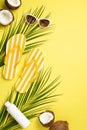 Summer rest concept. Top view vertical photo of yellow striped slippers sunglasses sunscreen bottle cracked coconuts and palm