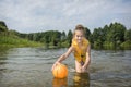 In summer, on the river, a girl in a vest plays with a ball.