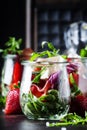 Summer salad with arugula, soft cheese, red strawberry and prosciutto in glass jars on black table, selective focus Royalty Free Stock Photo