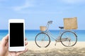 Summer sale concept, online shopping and delivery, smartphone in girlhand with bicycle with jute bag over blurred beach background Royalty Free Stock Photo