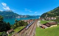 Summer scenery of beautiful Lake Lucerne on a sunny day, with a train traveling on the railway thru Sisikon Village