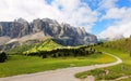 Summer scenery of majestic Sella Mountains & hiking trails winding in the green grassy valley on a cloudy sunny day