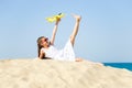 Cute happy little girl wearing sun eyeglasses and a white dress lying on the sandy beach by the sea and playi Royalty Free Stock Photo