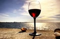 Summer seaside glass of red wine on beach stone and seashells nature panorama blue sky and sea water sunlight reflection romantic Royalty Free Stock Photo