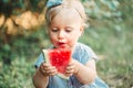 Summer seasonal picnic food. Cute baby girl eating ripe red watermelon in park. Funny child kid sitting on ground with fresh Royalty Free Stock Photo