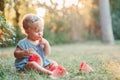 Summer seasonal picnic food. Cute Caucasian baby girl eating ripe red watermelon in park. Funny child kid sitting on ground with Royalty Free Stock Photo