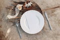 Summer setting with cutlery, dry palm leaf and porcelain plate. Coconut, silk ribbon and white oleander flowers on
