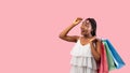 Summer shopping. Happy black woman with bags lifting sunglasses, looking at empty space on pink background Royalty Free Stock Photo