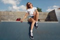 Summer. Skater Girl Sitting On Concrete Skate Ramp At Skatepark. Female Teenager In Casual Outfit With Skateboard.