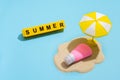 Summer skin care concept. Sunscreen on the sand and an umbrella from the sun on a blue background. Text from letters on yellow