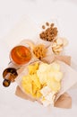 Summer snacks and lager beer in glass - nachos, croutons, chips, tortilla on craft paper on white wood background, top view. Royalty Free Stock Photo