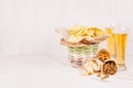 Summer snacks and lager beer in glass - nachos, croutons, chips, tortilla in rustic basket and paper corners on white wood backgr