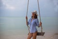 Summer solar portrait of fashion of a way of life of the young stylish woman,sitting on a swing on the beach,carrying lovely fashi Royalty Free Stock Photo