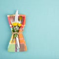 Summer or Spring Table Setting with teal tablecloth, silverware, and multicolor cloth napkin with yellow daisy flowers. Backgroun