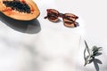 Summer stationery still life scene. Closeup of cut papaya fruit, olive branch and sunglasses in sunlight. White table Royalty Free Stock Photo