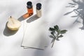 Summer stationery still life scene. Cut pear fruit, cosmetic oil, cream bottles and olive tree branch. White table