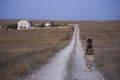 Summer steppe - a dark-haired girl with a backpack walks along the road that goes to the buildings of houses and beyond