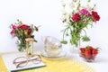 Summer still life: bouquets of wild flowers in various vases, strawberries in a glass cup, a yellow openwork napkin, a notebook, Royalty Free Stock Photo