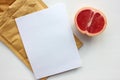 Summer still life with half of grapefruit, blank paper card and golden envelope on white background. Invitation mockup.