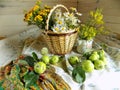 Summer still life made of wicker basket, wild flowers and green apples