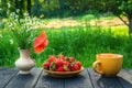 Summer still life of a plate with strawberries and coffee on a table with flowers. Summer morning or evening background Royalty Free Stock Photo
