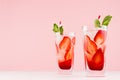 Summer strawberry lemonade with green mint, ice cubes, striped straw on elegant pastel pink wall, white wood table, copy space.