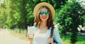 Summer sunny portrait beautiful smiling young woman with cup of coffee wearing a straw hat and backpack in the city park Royalty Free Stock Photo