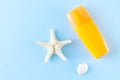 Summer sunscreen or spray next to sea shell and starfish on blue background top view