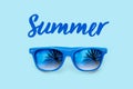 Summer textured blue text and blue sunglasses with palm trees reflections isolated in a light blue background