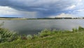 In summer, there is a storm cloud over the lake and it rains. The water ripples in the wind. Meadow flowers bloom on the grassy sh