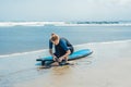 Summer time and active rest concept. Young surfer woman beginner fastens leash across leg, going to surf on big barral