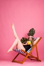 Summer time girl sitting in beach chair on pink background with copy space