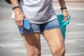 Summer tourist - Closeup of woman in blue jean shorts walking with fitness bracelet and phone in her hand and plastic bag from