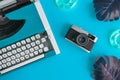 Flat lay of typewriter with retro camera and inflatable floats with monstera leaves abstract on turquoise background