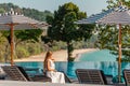 Traveler woman in white dress and hat sitting on sun lounger near swimming pool Royalty Free Stock Photo