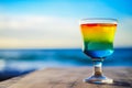 Glass of colourful cold fresh summer cocktail on wooden table with ocean view on background Royalty Free Stock Photo