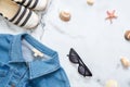 Summer vacation composition. Fashionable jeans jacket, sunglasses, striped sandals, seashells, sea star on marble background. Wome