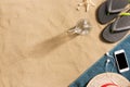 Summer vacation composition. Flip flops, hat, smartphone and glass of water on sand background