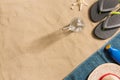 Summer vacation composition. Flip flops, hat, sun cream and glass of water on sand background