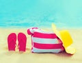 Summer vacation concept - bag with straw hat and flip flops on beach on blue sea background Royalty Free Stock Photo