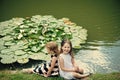 Summer vacation concept. Girls sit on grass at pond with water lily flowers Royalty Free Stock Photo